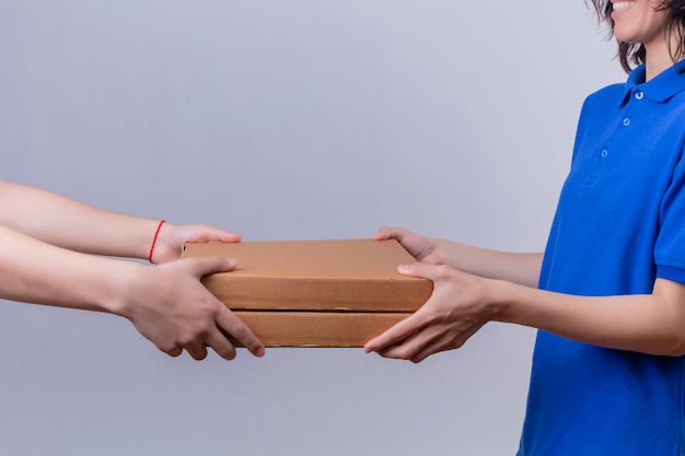 Bezorgingsmeisje in blauw uniform dat pizzadozen geeft aan u klant over geïsoleerde witte ruimte