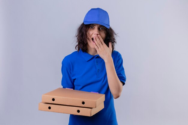 Bezorgingsmeisje in blauw uniform en pet die pizzadozen houden die verbaasd kijken die mond met hand status bedekken