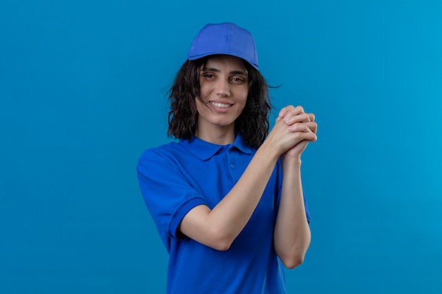 Bezorgingsmeisje in blauw uniform en pet die zich met een gebaar van groepswerk bevindend vriendschappelijk op geïsoleerd blauw glimlachen