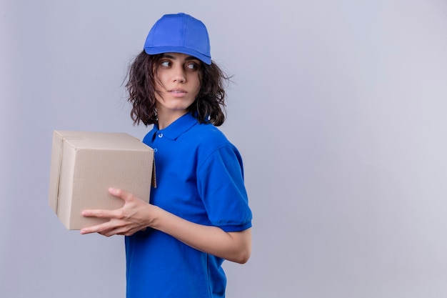 Bezorgingsmeisje in blauw uniform en pet met doospakket dat zijwaarts met ernstig gezicht wegkijkt