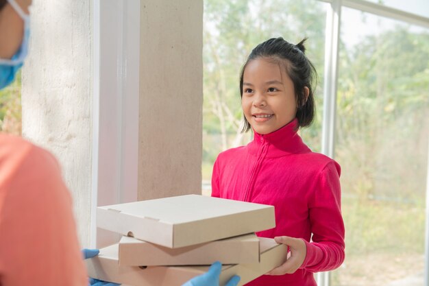 Bezorgservice in t-shirt, in beschermend masker en handschoenen die eten bestellen, drie pizzadozen voor het huis houden, vrouw die dozen van bezorger accepteert tijdens COVID-19-uitbraak.