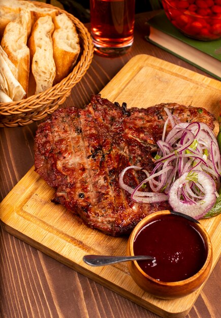 Biefstuk met barbecue, bbq saus en kruiden, ui salade, gegrilde peper en tomaat op houten plaat
