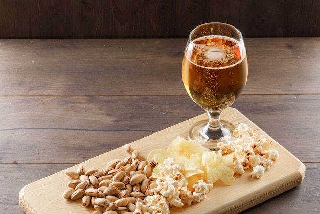 Gratis foto bier met snack in een drinkbekerglas op houten en scherpe raadslijst, hoge hoekmening.