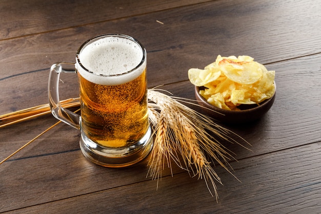 Bier met tarwe oren, chips in een glas op houten tafel, hoge hoek bekeken.