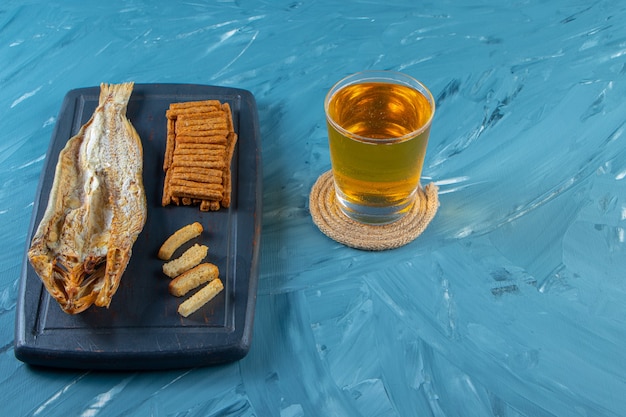 Bierpul naast gedroogde vis en croutons op een dienblad, op de blauwe achtergrond.