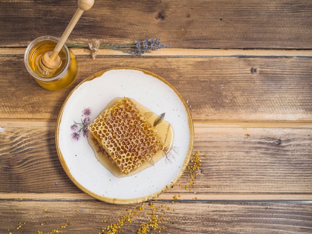 Bijenpollen; honingpot en honingraat stuk op witte plaat over de tafel