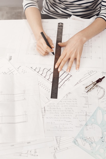 Bijgesneden bovenaanzicht van jonge mooie vrouwelijke architect handen doen blauwdrukken met liniaal en pen op witte tafel in naaiatelier ruimte. Bedrijfsconcept