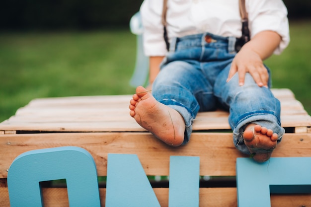 Gratis foto bijgesneden foto van een schattig kind met een wit overhemd en een spijkerbroek en poserend met blote voeten in het gras
