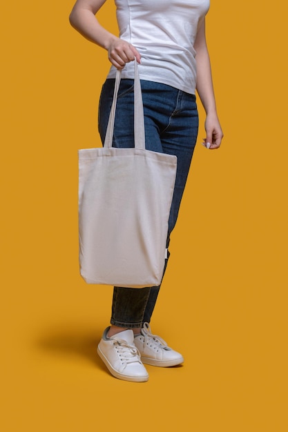 Bijgesneden foto van een vrouw gekleed in een t-shirt en spijkerbroek met haar trendy carry-all in één hand