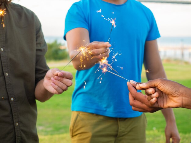 Bijgesneden opname van jonge mensen met brandende Bengalen lichten. Mannelijke handen met sparkles. Concept van viering