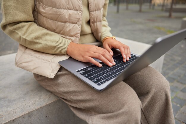 Bijgesneden opname van onherkenbare vrouwelijke blogger typen tekstpublicatie op draagbare laptopcomputer werkt op afstand buitenshuis gekleed in casual kleding toetsenborden op modern apparaat bereidt zich voor op examens