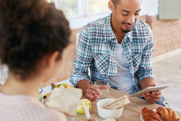 Bijgesneden schot van knappe donkere man blij met goed nieuws van internet, heeft lunch, drinkt water.