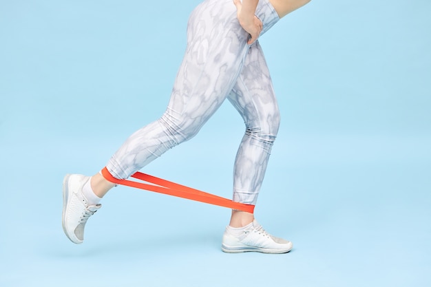 Bijgesneden schot van onherkenbare sportvrouw in legging en sneakers die traint met behulp van een weerstandsband om perfecte billen te krijgen, benen te trainen, aan spieren te werken, bilspieren en hamstrings te versterken