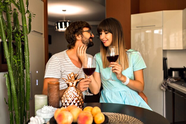 Binnen romantisch familieportret van vrij jong getrouwd stel romantische avond samen doorbrengen, thuis drinken van rode wijn en ontspannen.