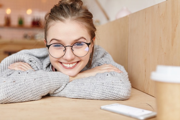 Binnen schot van dromerige aanbiddelijke vrouw die ronde bril draagt