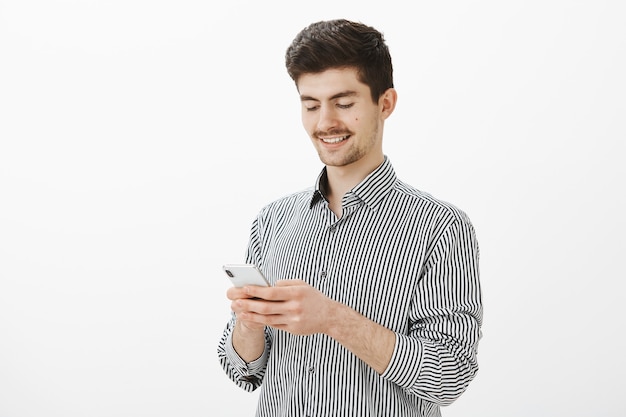 Binnen schot van gerichte tevreden aantrekkelijke man met baard en snor, smartphone vasthouden, scherm kijken met tevreden, gelukkige glimlach, lawer berichten over echtscheiding