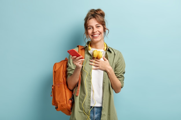 Binnen schot van tevreden Europese student blij om een felicitatiebericht te ontvangen na het behalen van het examen, houdt de handpalm op de borst, toont dankbaarheid, luistert naar muziek met een koptelefoon, draagt stijlvolle kleding