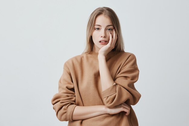 Binnenopname van een bedachtzame mooie vrouw met lang blond haar, kijkt naar voren met peinzende uitdrukkingen, plant iets voor de komende weekenden