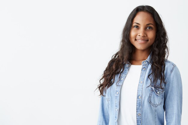 Binnenportret van het mooie Afro-Amerikaanse donkerbruine jonge vrouw vrolijk glimlachen, tonend haar witte tanden, voelend gelukkig en onbezorgd.