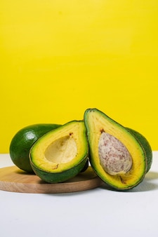 Biologische avocado met de helften van de zaadavocado en heel fruit op gele witte achtergrond voedselconcept
