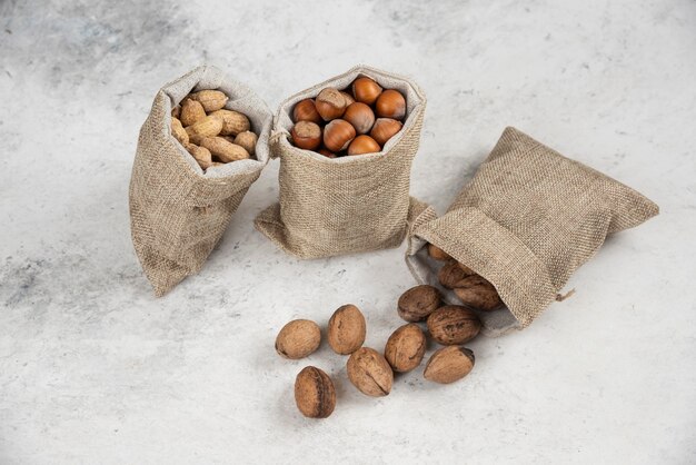 Biologische gepelde hazelnoten, pinda's en walnoten in jute op marmeren tafel.