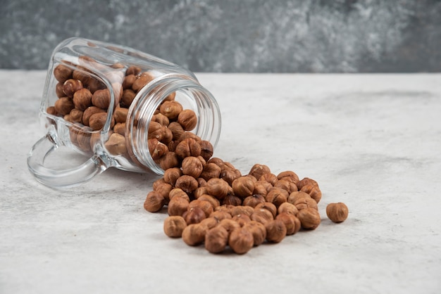 Biologische hazelnootpitten uit glazen pot op marmeren tafel.