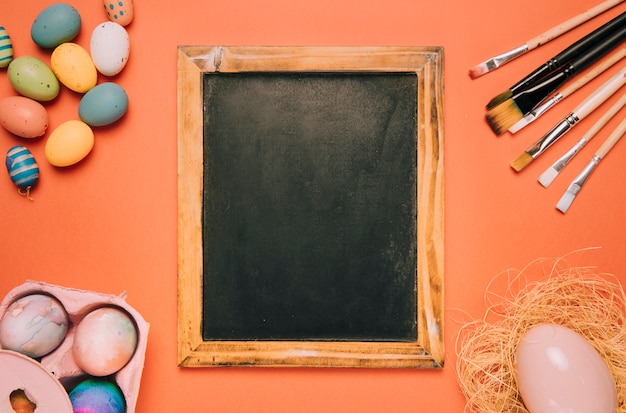 Blackboard met verfborstels; paaseieren op een oranje achtergrond