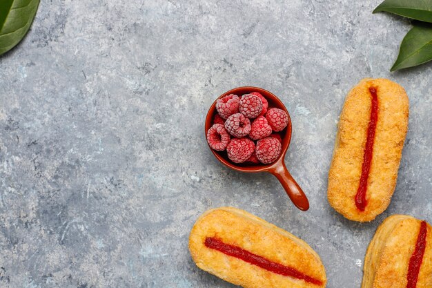 Bladerdeegkoekjes met frambozenjam en bevroren frambozen op licht