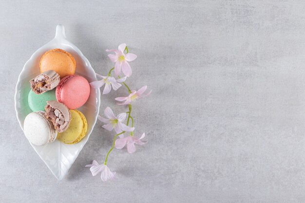 Bladvormige plaat van kleurrijke zoete bitterkoekjes met bloemen op stenen tafel.