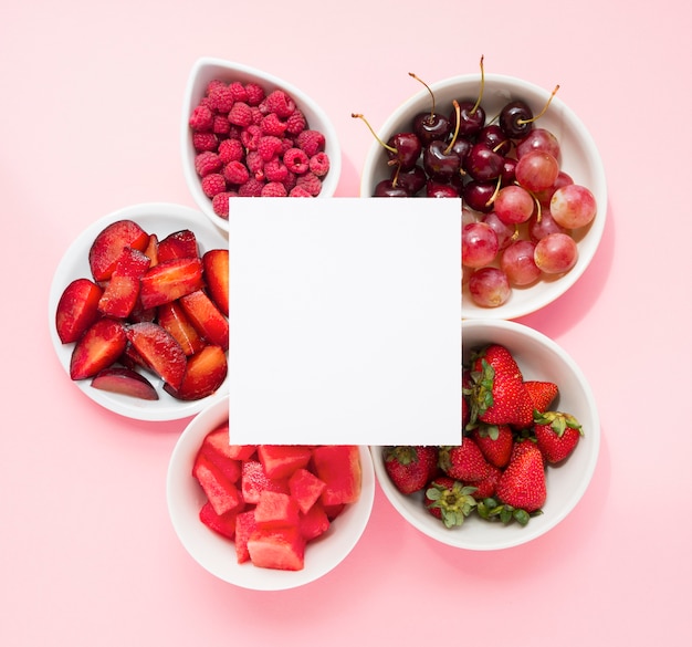 Blanco pagina over de frambozen; pruimen; watermeloen; aardbeien; kersen; druiven en aardbeien op roze achtergrond