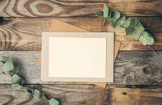 Blanco papier en envelop op houten ondergrond met eucalyptustakjes plat gelegd