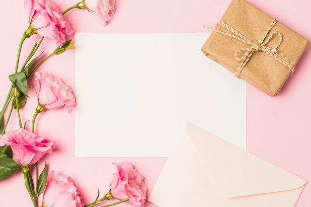 Blanco papier met envelop; verse roze bloem en bruin gewikkeld geschenk doos over roze achtergrond