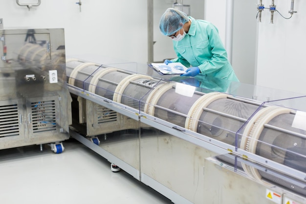 Blanke fabrieksarbeider in blauw laboratoriumpak met tablet in handen buigt op machinecontrolemetingen