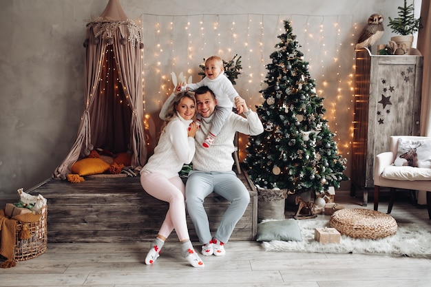 Blanke familie speelt thuis met hun jonge kind in een woonkamer met een kerstboom