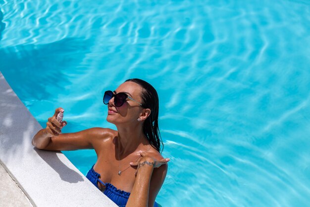 Blanke gebruinde vrouw glanzende bronzen huid bij zwembad in blauwe bikini op zonnige dag