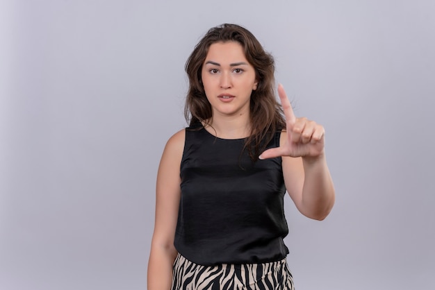 Blanke jonge vrouw, gekleed in zwart onderhemd met haar vinger omhoog op een witte muur