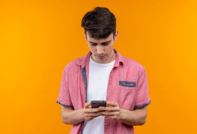 Blanke jongeman met roze shirt nummer op de telefoon op geïsoleerde oranje muur dragen