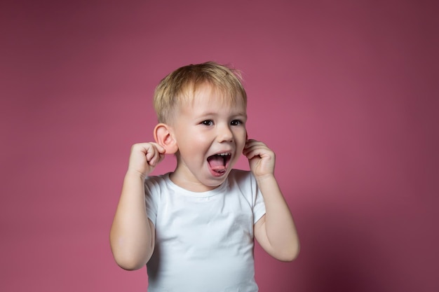 Blanke jongen van 3 jaar oud maakt gezichten, toont tong, kijkt naar camera op roze achtergrond