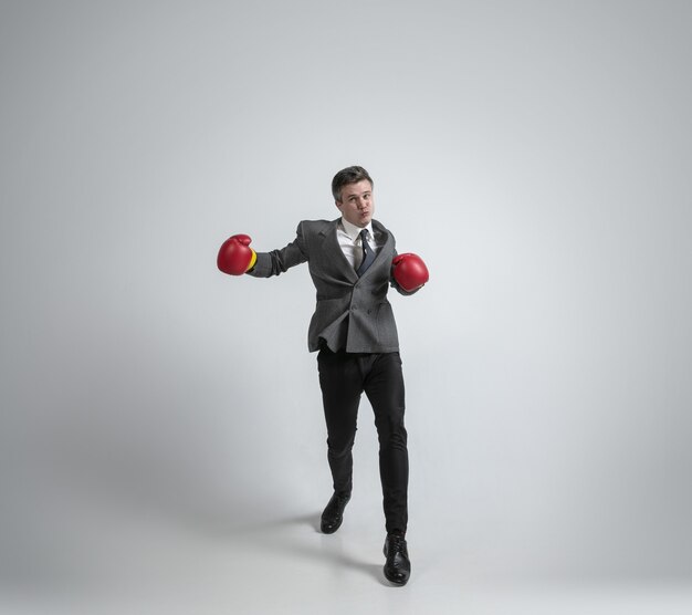 Blanke man in office kleren boksen met twee rode handschoenen op grijze achtergrond.
