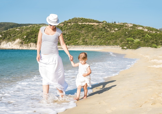 Blanke moeder die overdag met haar dochter op het strand loopt