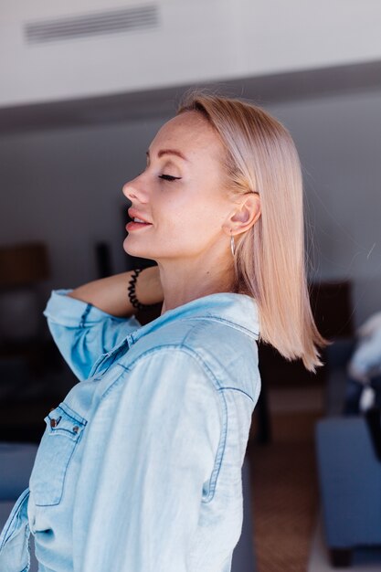 Blanke mooie blonde kort haar vrouw in denim jasje haar borstelen met roze haarborstel thuis