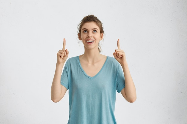 Blanke mooie vrouw met een positieve uitdrukking glimlachend breed opzoeken met haar blauwe ogen aangeeft op iets