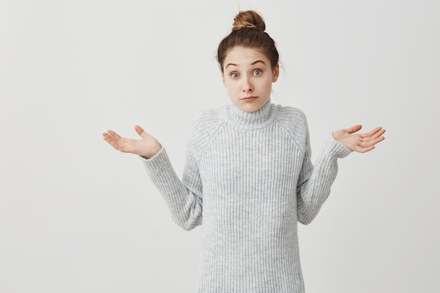 Blanke vrouw overgeven handen met onzekerheid op het gezicht. Vrouwelijke startende ondernemer die zich gedraagt als heb geen idee of geeft niet om witte muur. Emoties concept