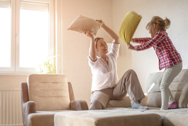 Blanke vrouw speelt met kussens met haar 6-jarige dochter op de bank in hun huis