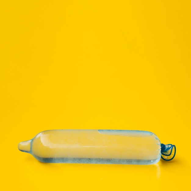 Blauw condoom dat met water op gele achtergrond wordt gevuld