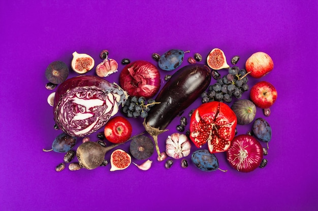 Blauw, rood en paars voer. culinaire achtergrond van groenten en fruit. verse vijgen, pruimen, ui, aubergine, druiven, kool, appel, knoflook, kornoelje, granaatappel, rode biet. violette achtergrond, plat gelegd