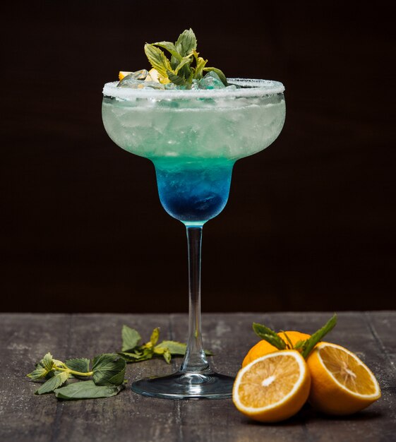 Blauwe en groene cocktail gegarneerd met citroen en mint in glas met lange steel