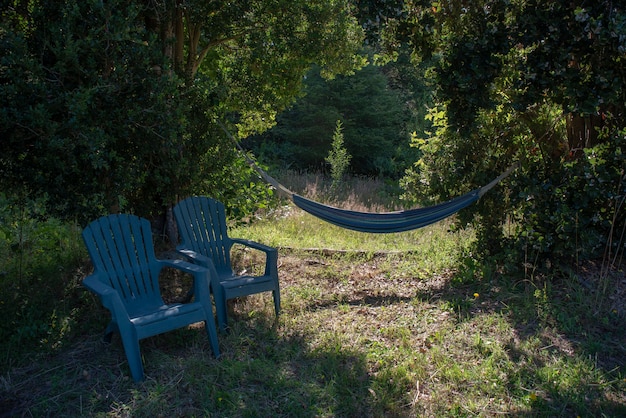 Blauwe hangmat vastgemaakt aan bomen met blauwe plastic stoelen aan de zijkant in een groen bos