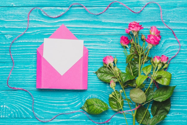 Blauwe houten oppervlak met lege nota over envelop en paarse bloemen