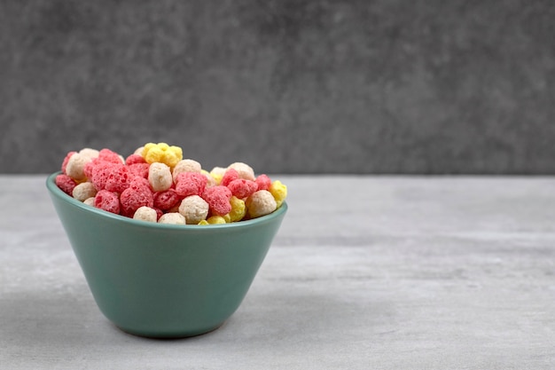 Blauwe kom met kleurrijke cornflakes op stenen tafel.